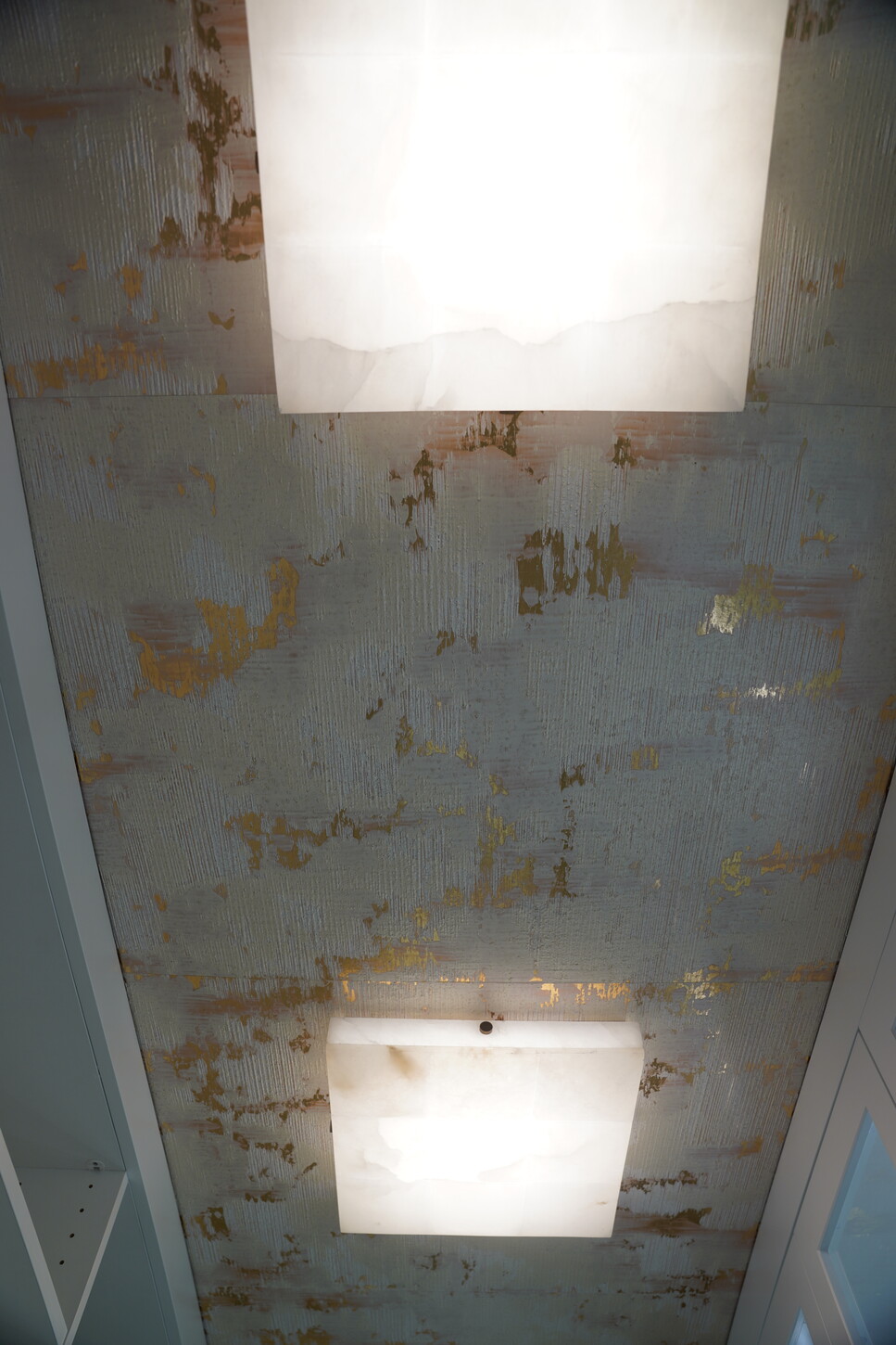 Textured metallic ceiling detail with alabaster flush-mount lighting in a custom closet