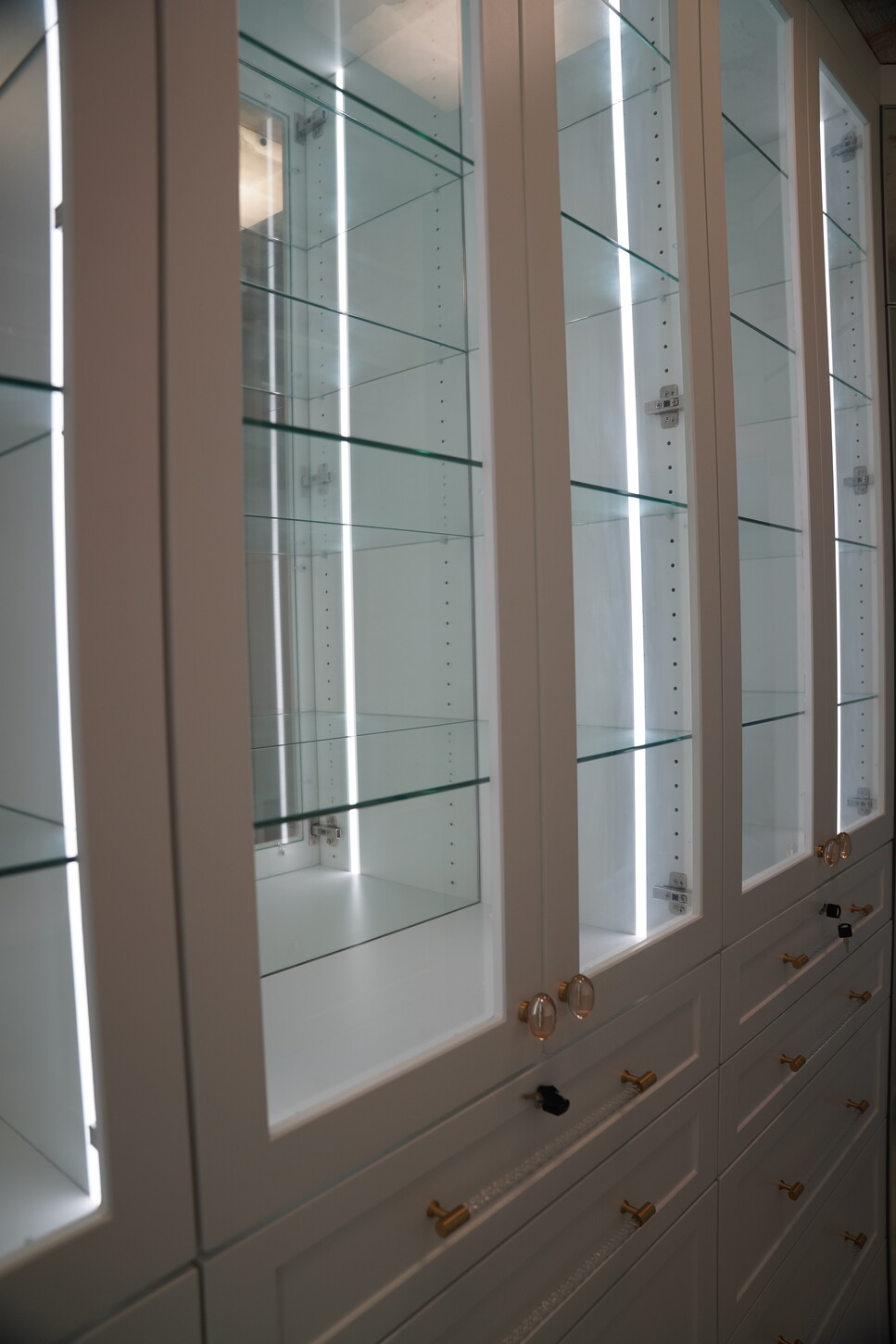 White custom closet display cabinetry with glass fronts and integrated LED lighting