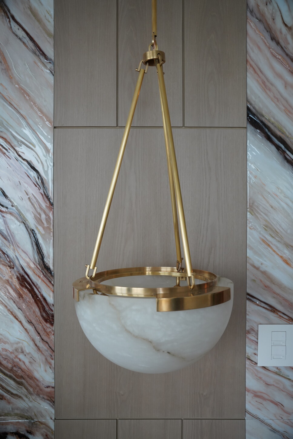Alabaster bowl pendant light with a brass frame beside an imitation stone accent wall