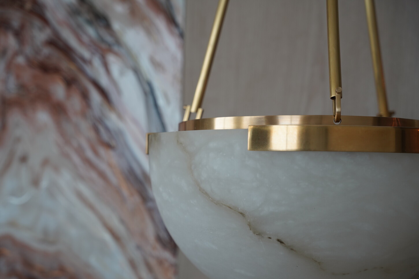 Alabaster pendant light detail with a brass ring against an imitation stone wall panel