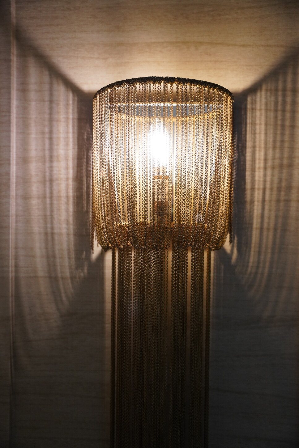 Sculptural gold chain-link wall sconce against a wood-paneled wall