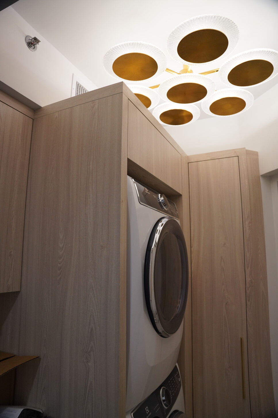 Custom laundry room cabinetry concealing a washer and dryer with a sculptural gold ceiling fixture