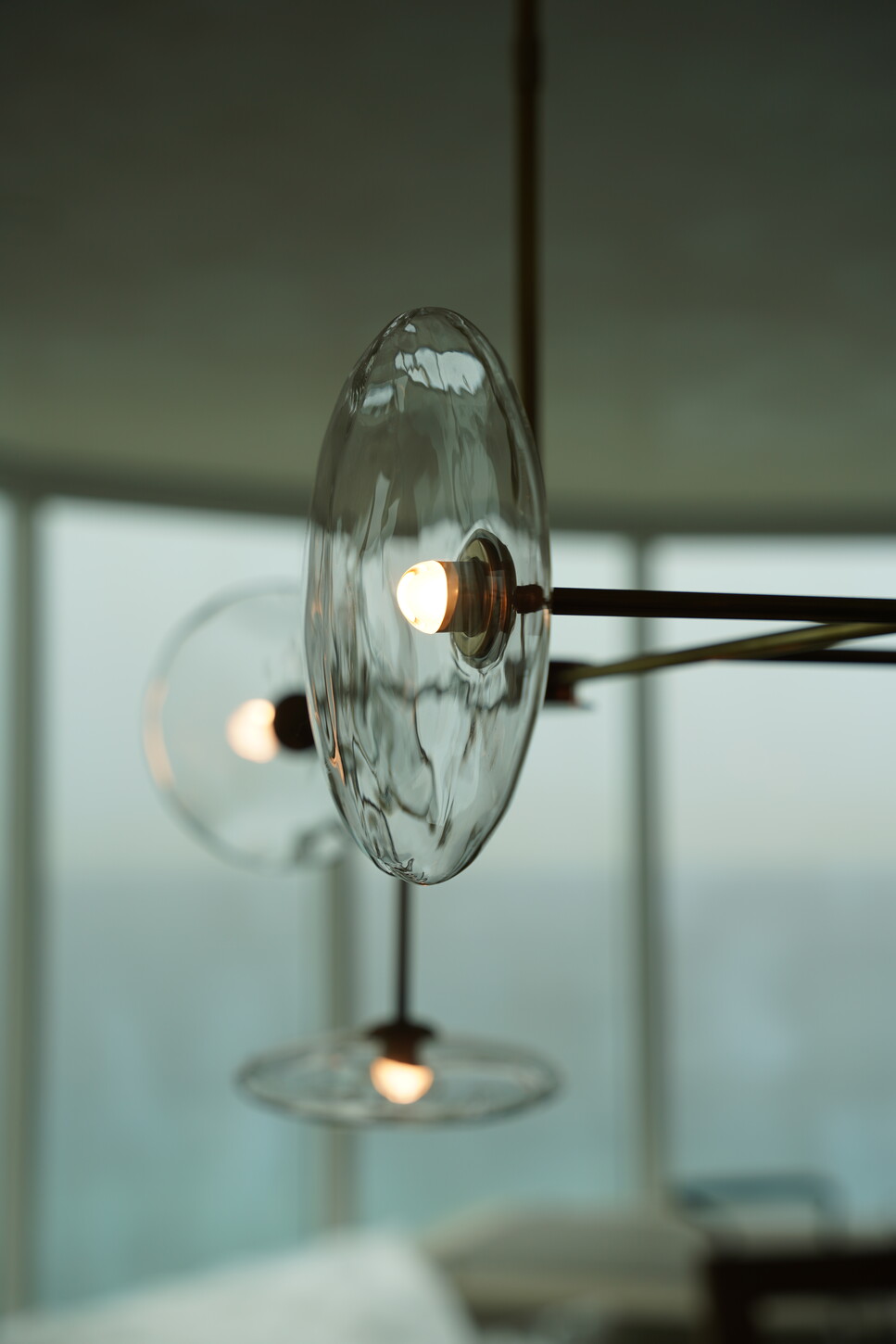 Sculptural glass-disc chandelier with brass fittings in front of an ocean-view window