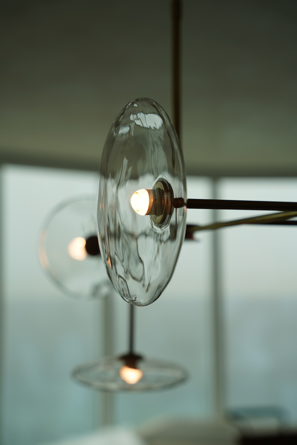 Glass-disc chandelier detail with brass hardware overlooking the ocean