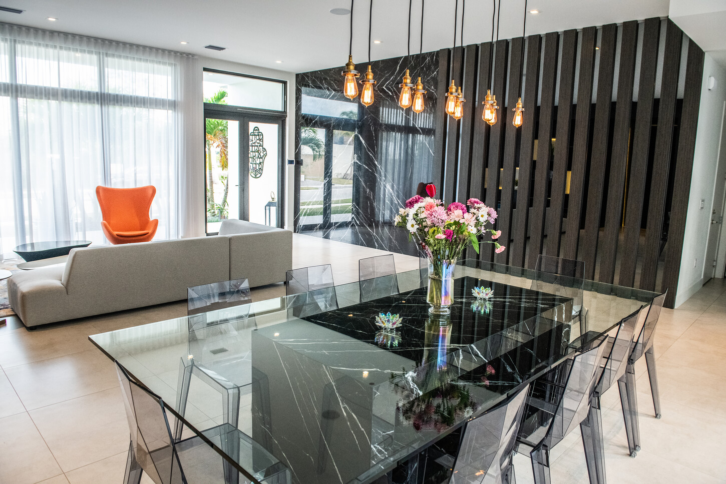 Dining area with custom marble-base glass table, orange accent chairs, and sheer curtains in Weston Botanico residence