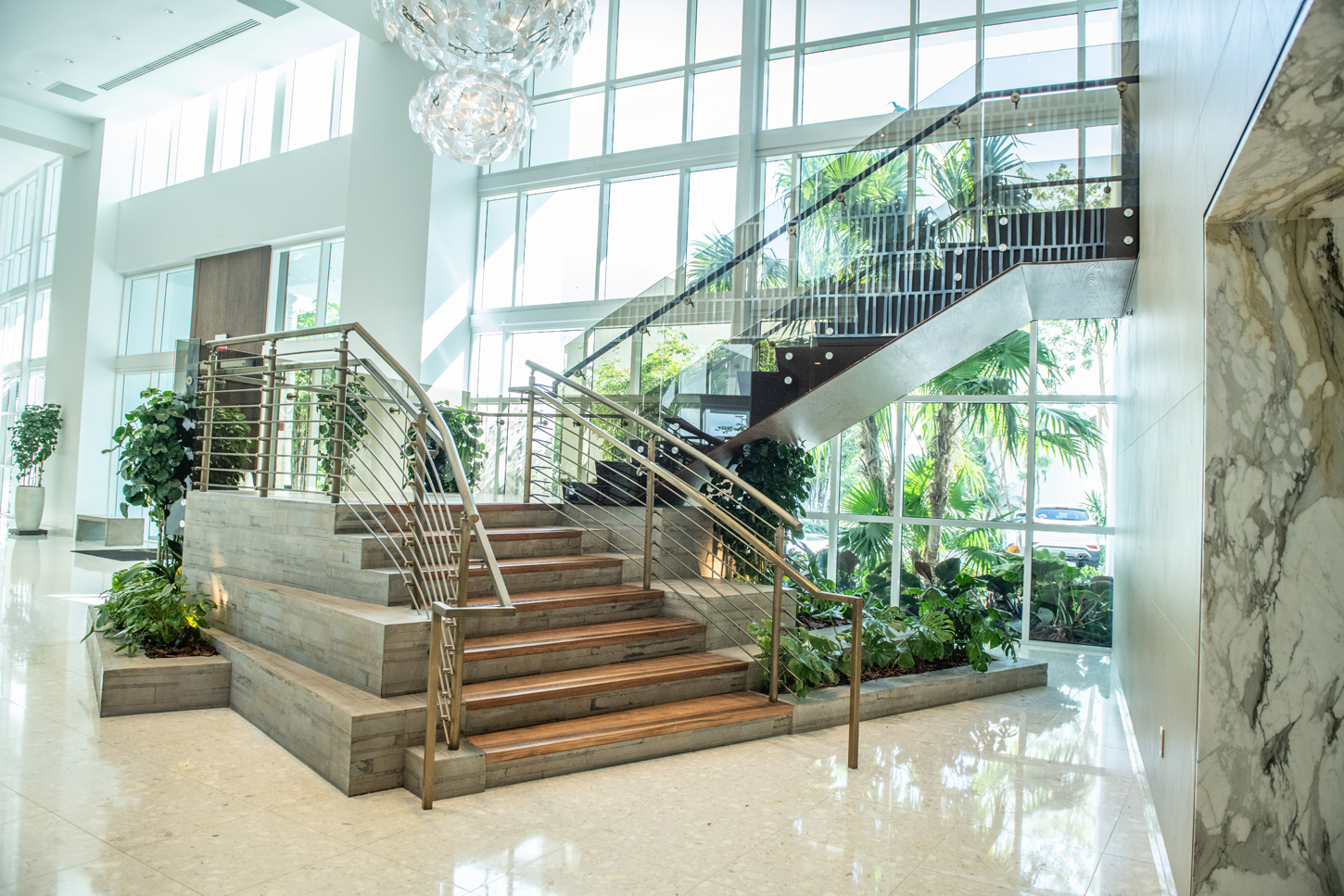 Grand staircase and lobby with marble finishes and glass railings, showcasing CM Custom Design craftsmanship