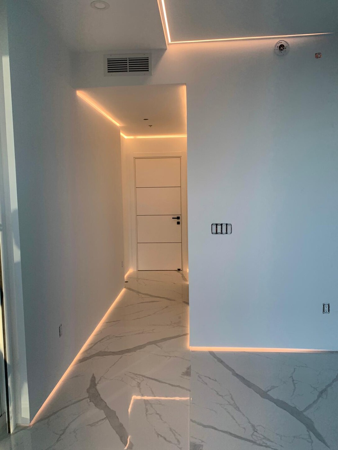 Hallway with floating LED cove lighting along the ceiling and floor transitions in this Midtown waterfront residence