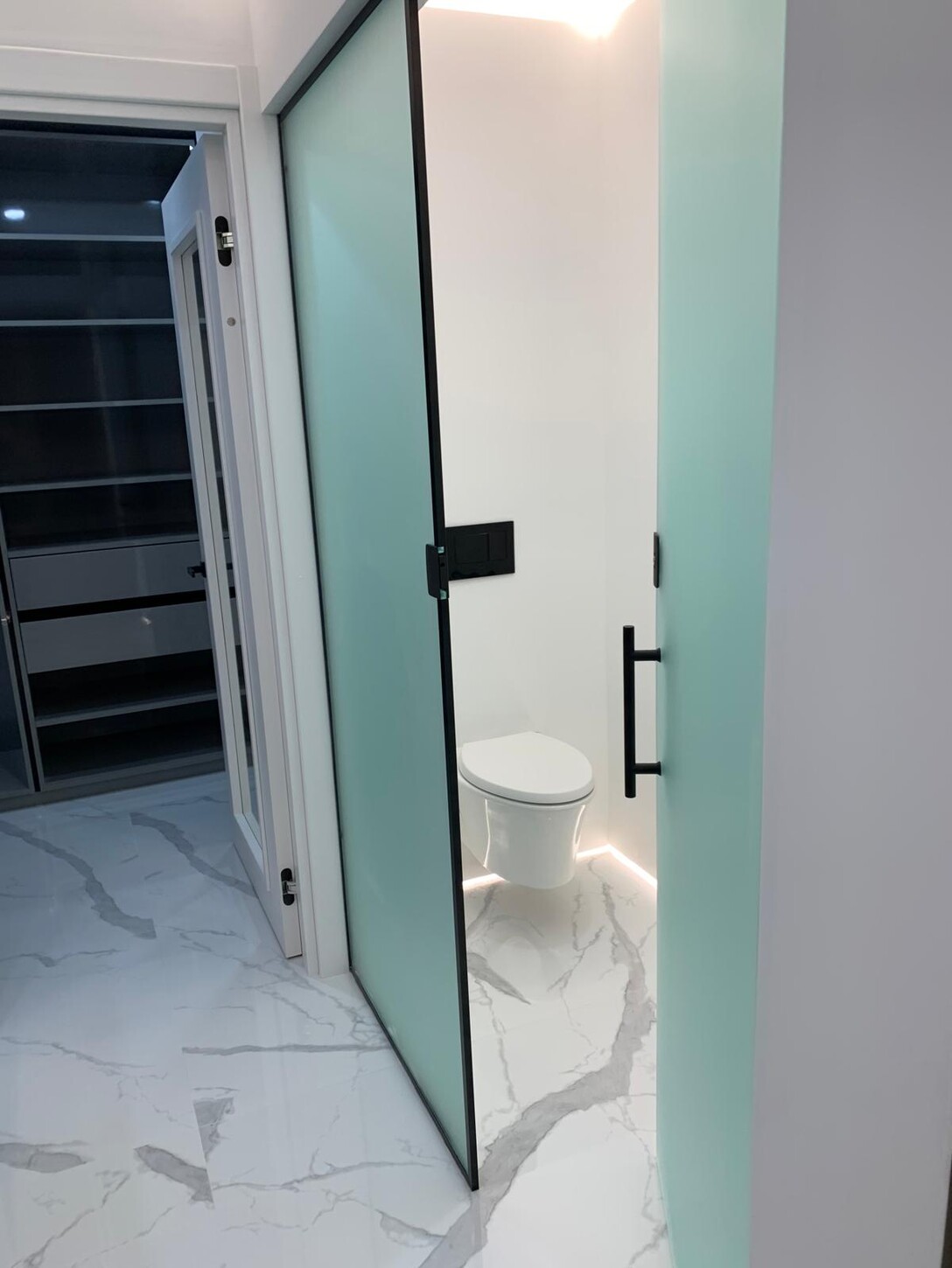 Powder room with a frosted glass sliding door and wall-mounted floating toilet in this Midtown waterfront residence