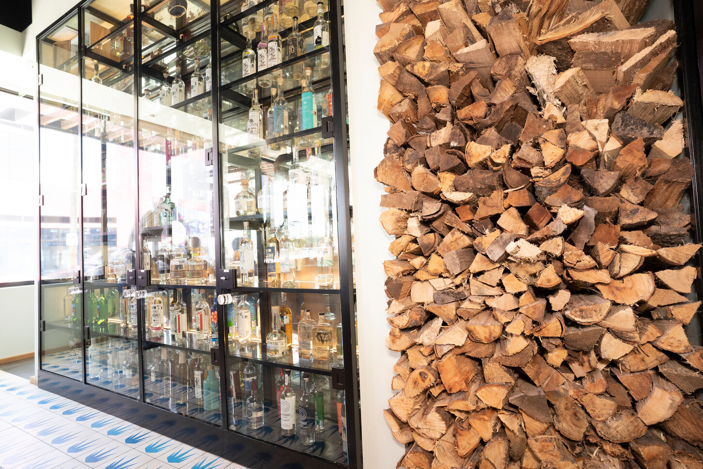 Glass bottle cabinet in front of a stacked firewood feature wall at Bakan Wynwood in Miami