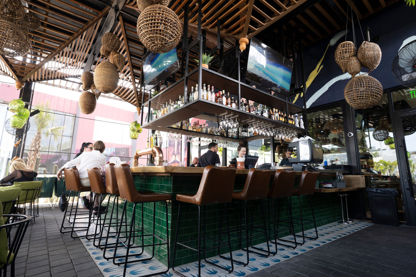 Outdoor terrace bar with suspended steel shelving and rattan lights at Bakan Wynwood in Miami