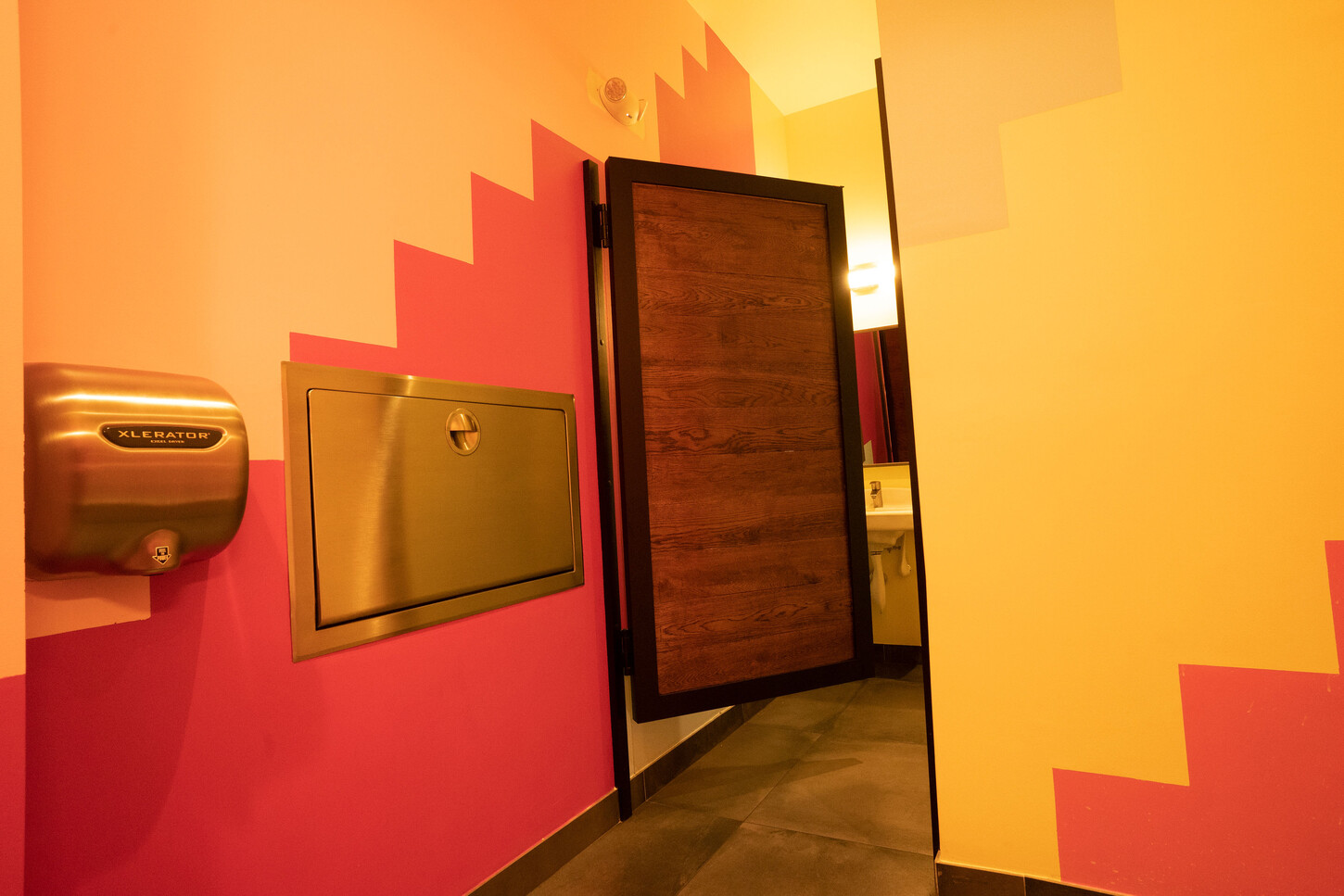 Restaurant restroom with a custom wood door and a geometric wall at Bakan Wynwood in Miami