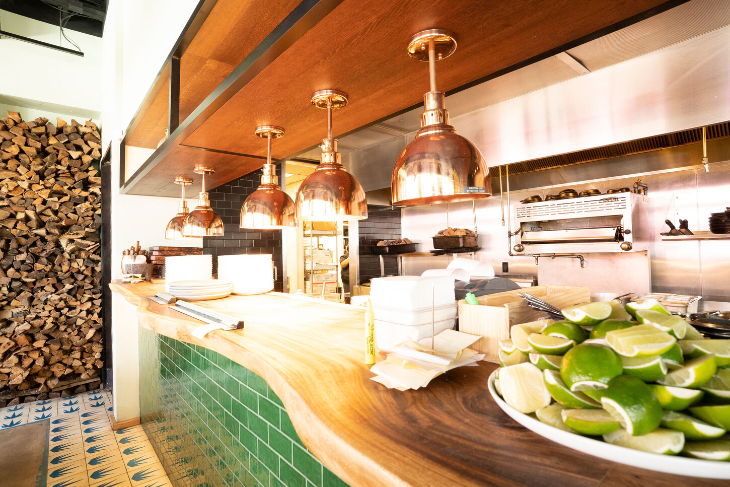 Custom counter with copper pendant lights and a firewood backdrop at Bakan Wynwood restaurant in Miami