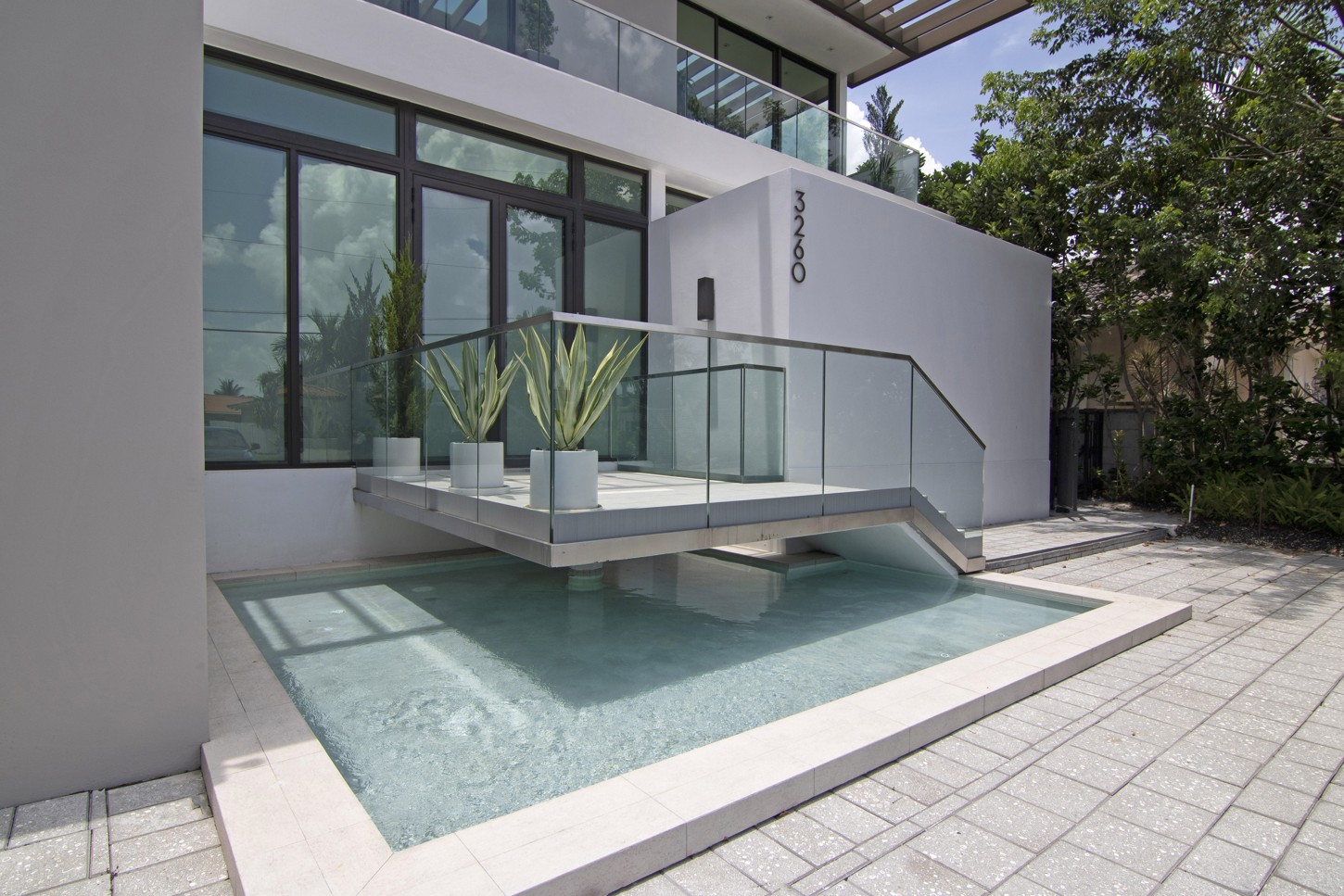 Glass railing bridge over a reflecting pool at the entry of a modern North Miami home