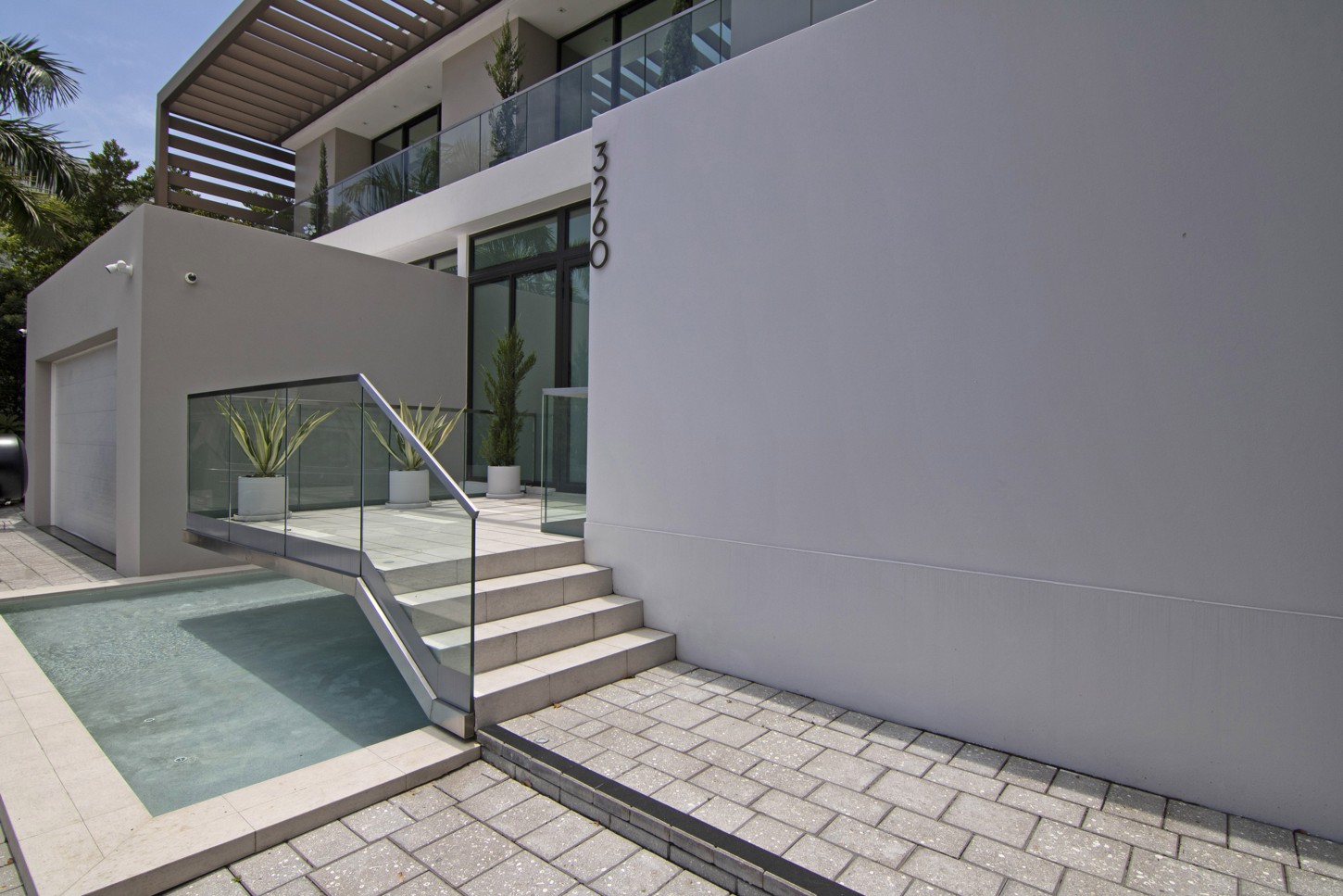 Entry stairs with glass railing beside a reflecting pool at a North Miami residence