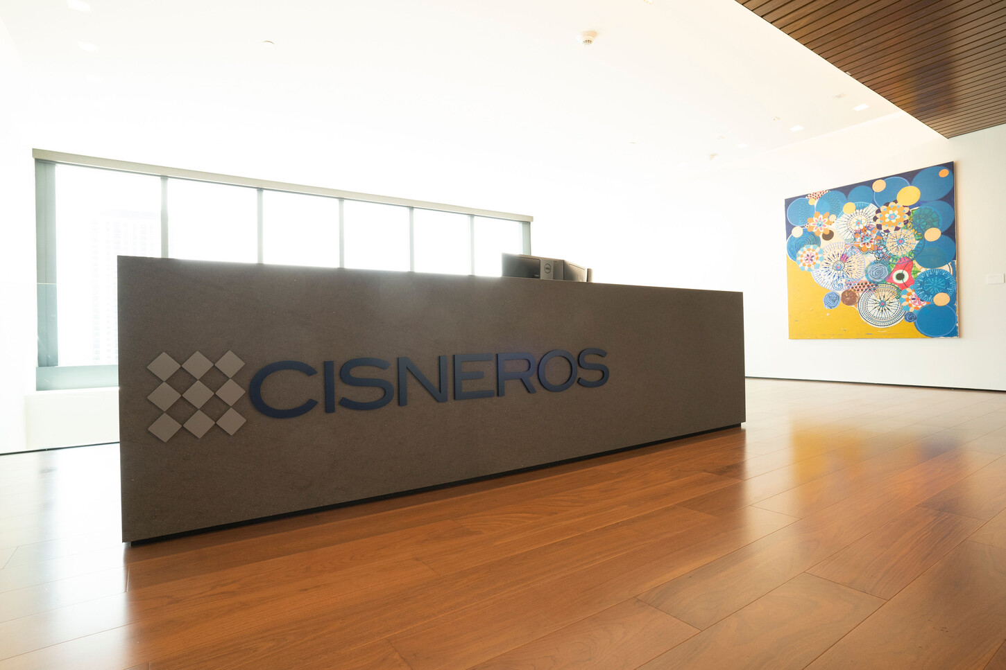 Custom reception desk on a wood floor beside colorful artwork in a Miami office lobby