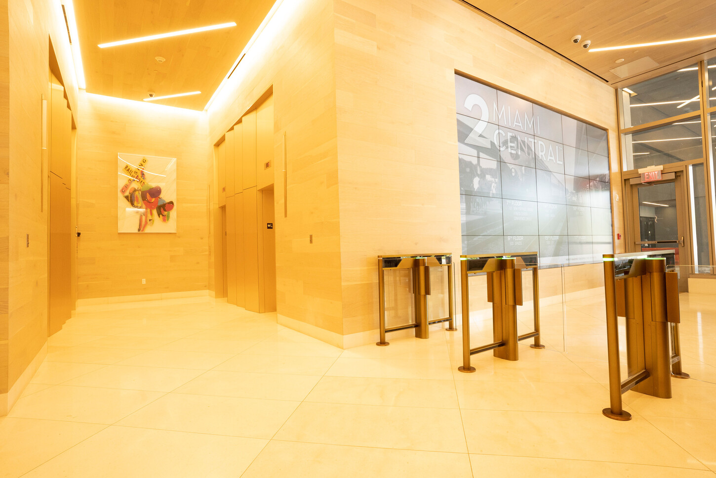Wood-clad elevator lobby walls with warm linear lighting and turnstiles in a Miami high-rise