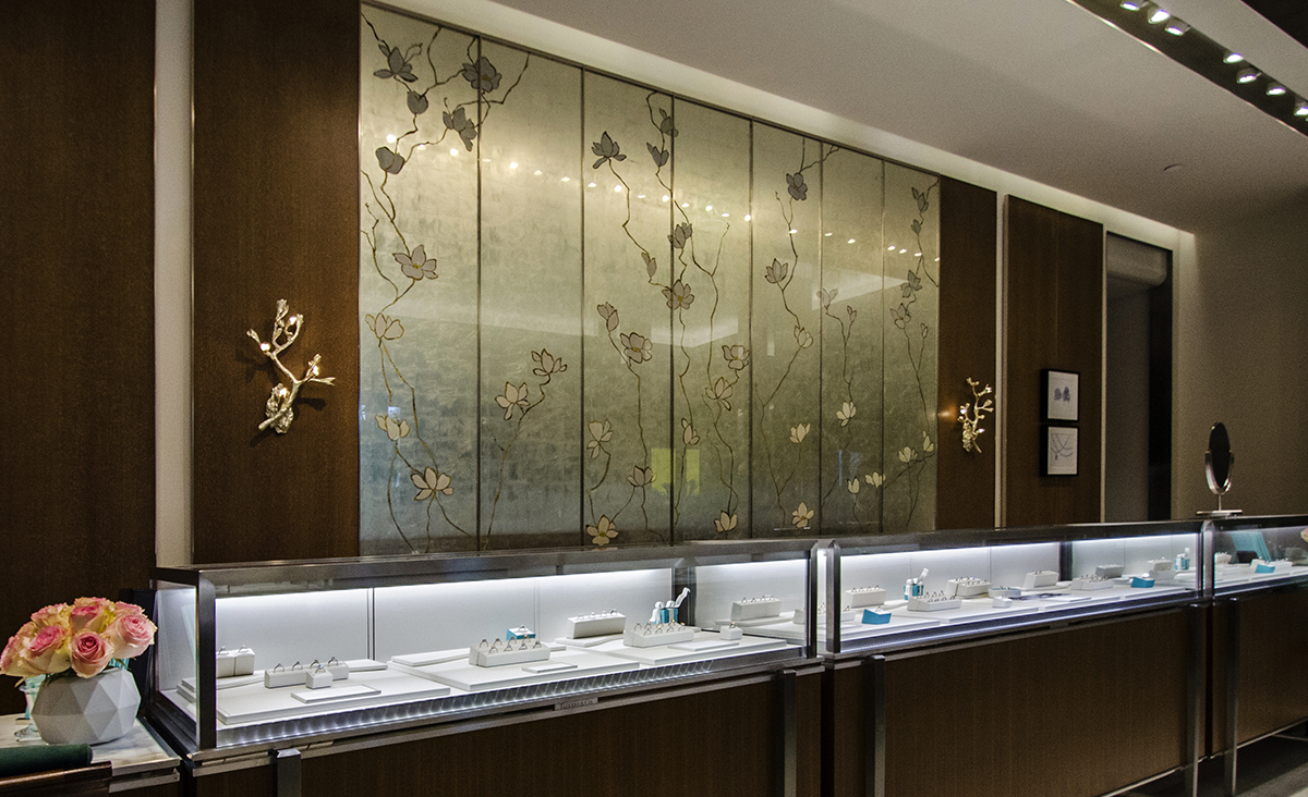 Jewelry display cases below a custom floral wall panel framed by wood paneling at Tiffany, Bal Harbour Shops